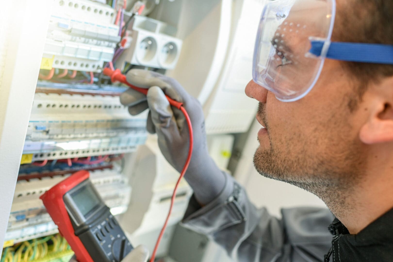 A man in safety glasses and gloves working on electrical equipment.