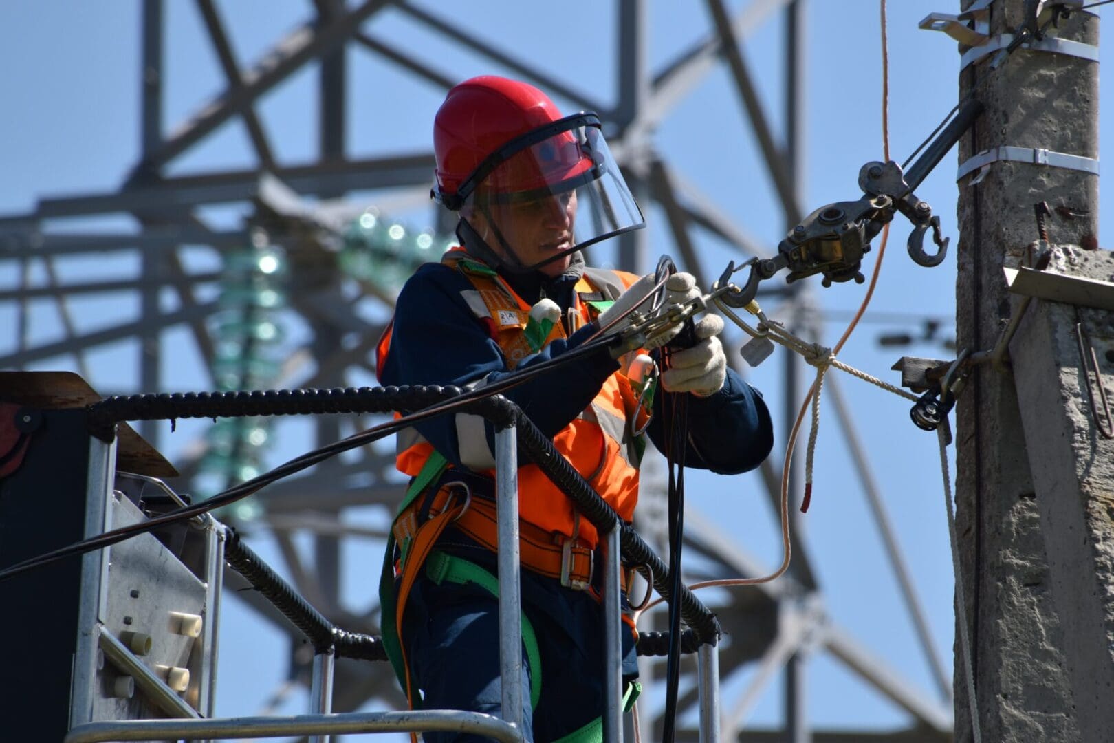 A man in an orange vest and hard hat working on wires.